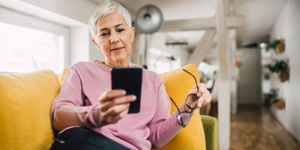 Woman on couch looking at phone while holding glasses