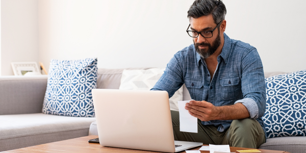 Man in glasses paying bills on his couch