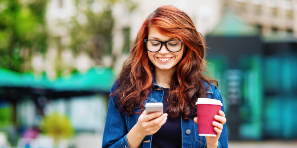Girl with glasses blocks debit card on phone while holding coffee